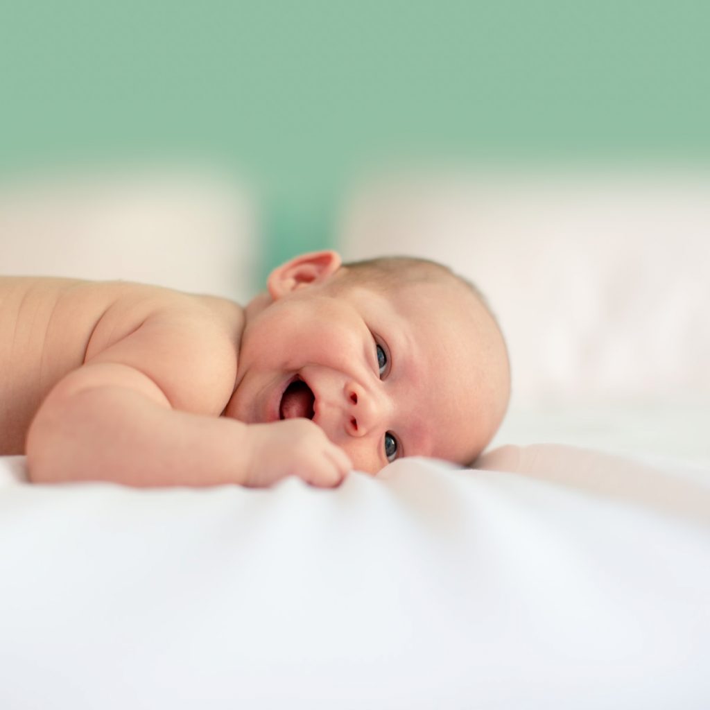 Un bébé qui sourit, étendu sur son lit après un massage bébé